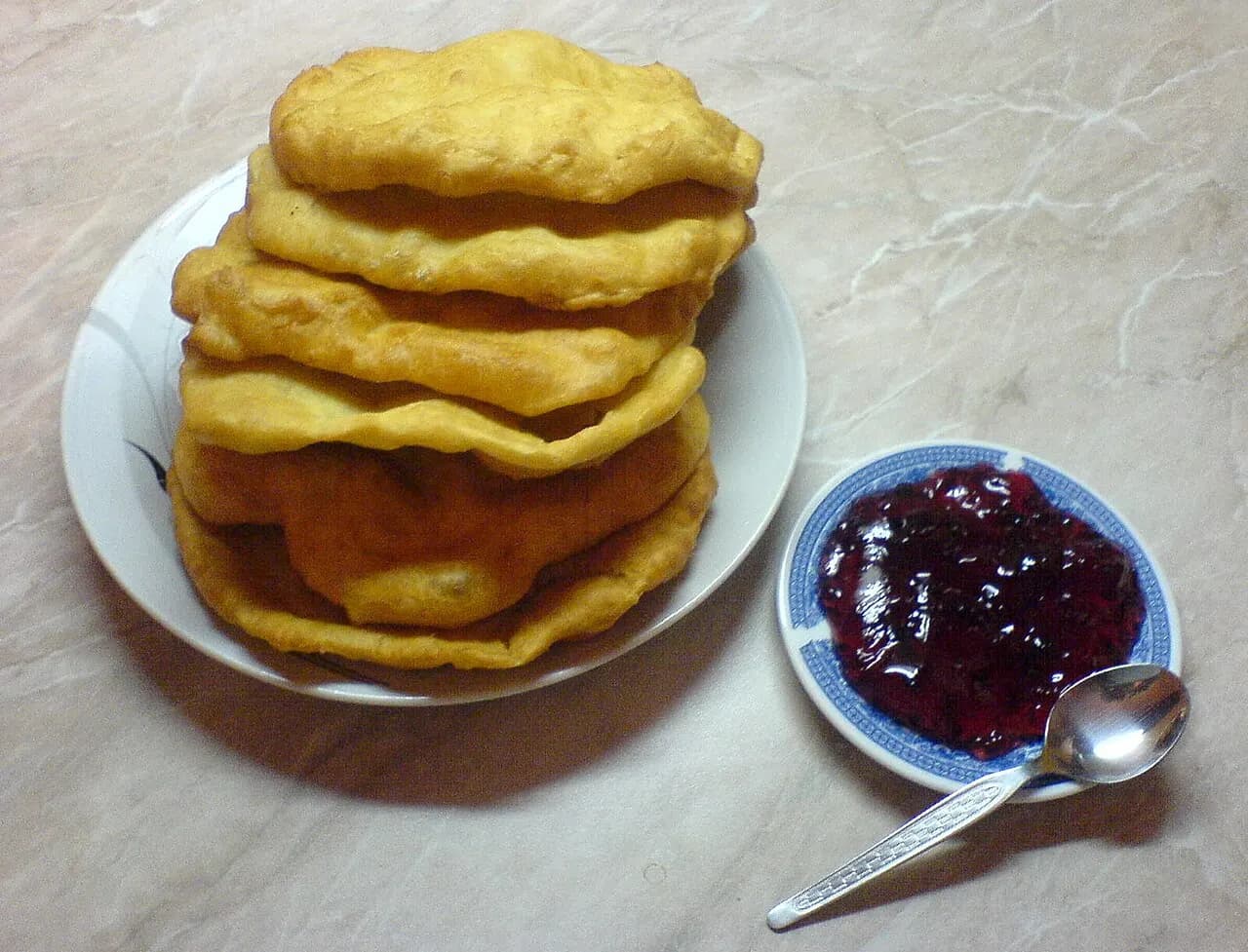 A stack of fried mekitsi on a plate served with a saucer of jam