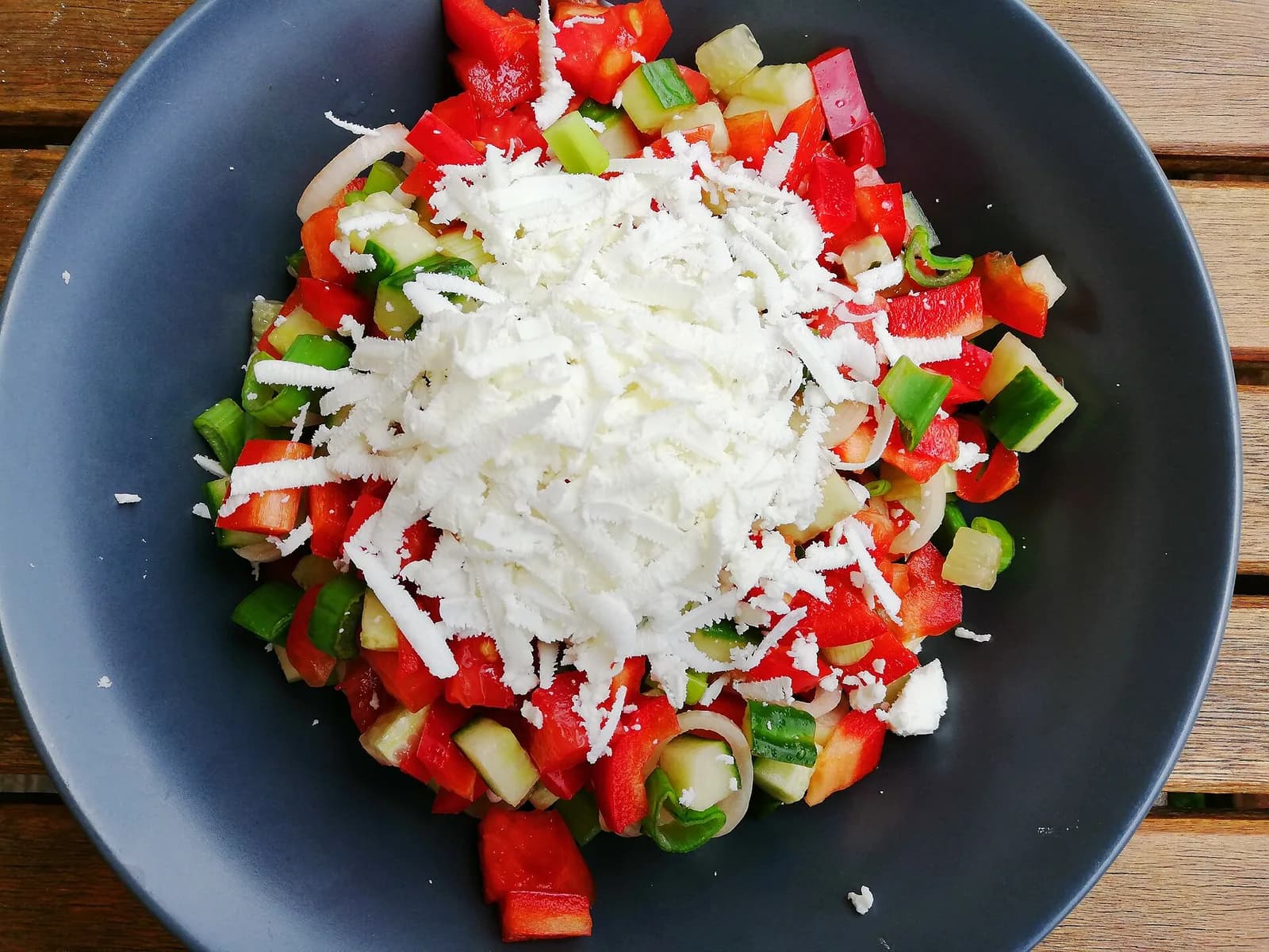 A bowl of Shopska salad with tomatoes, cucumber, peppers, and grated white cheese